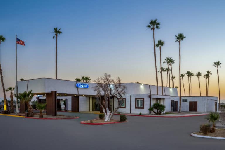 Atlas Hospitality Travelodge Imperial hotel exterior with palm trees at sunset.