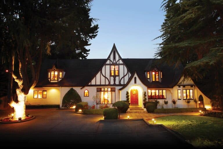 Elegant Tudor-style hotel illuminated at night with warm lighting and lush landscaping.