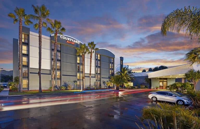 Modern hotel building with palm trees at sunset, part of Atlas Hospitality group.